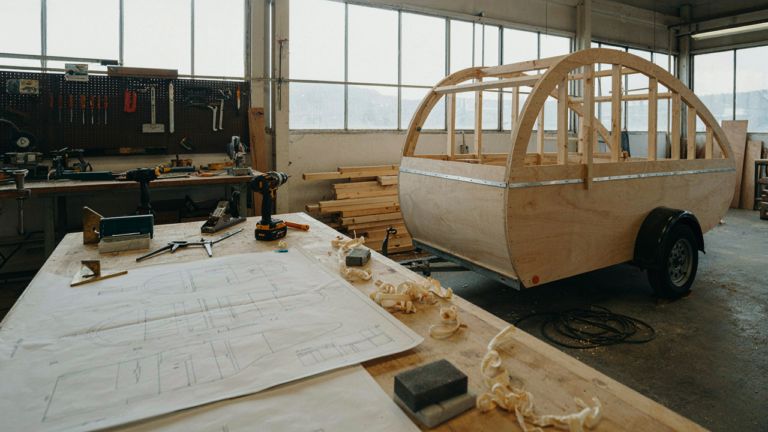 A partially built teardrop trailer in a bright workshop with tools and wood.
