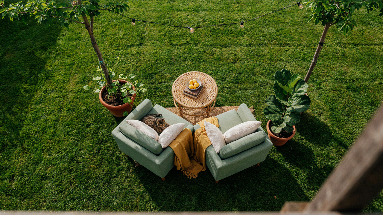 A cozy small backyard seating area sits on a patio next to a green lawn.