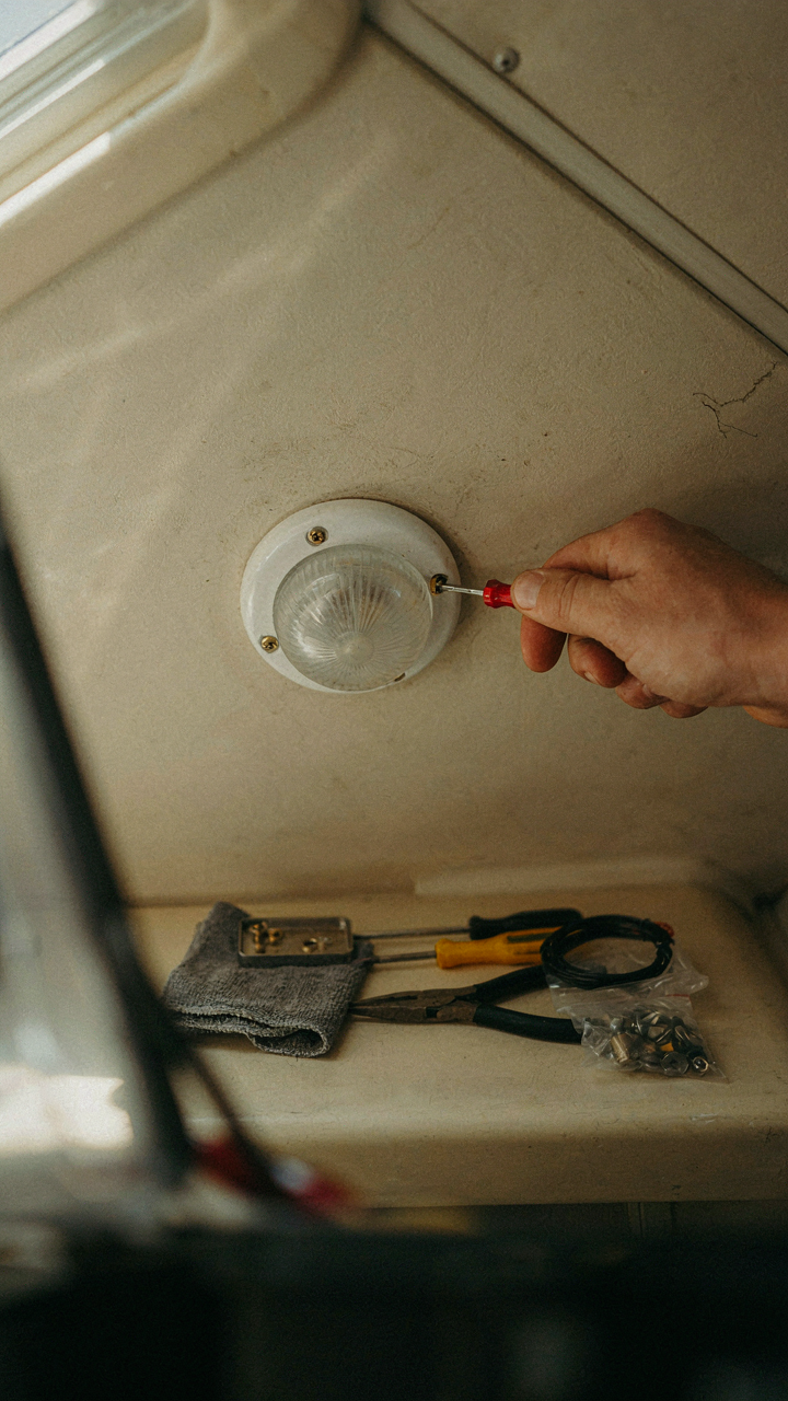 A hand carefully removes a small screw from an RV light fixture.