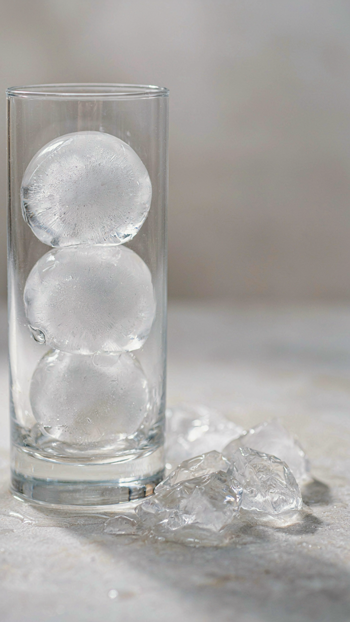 Large, clear round ice cubes fill a glass, next to small ice chips.