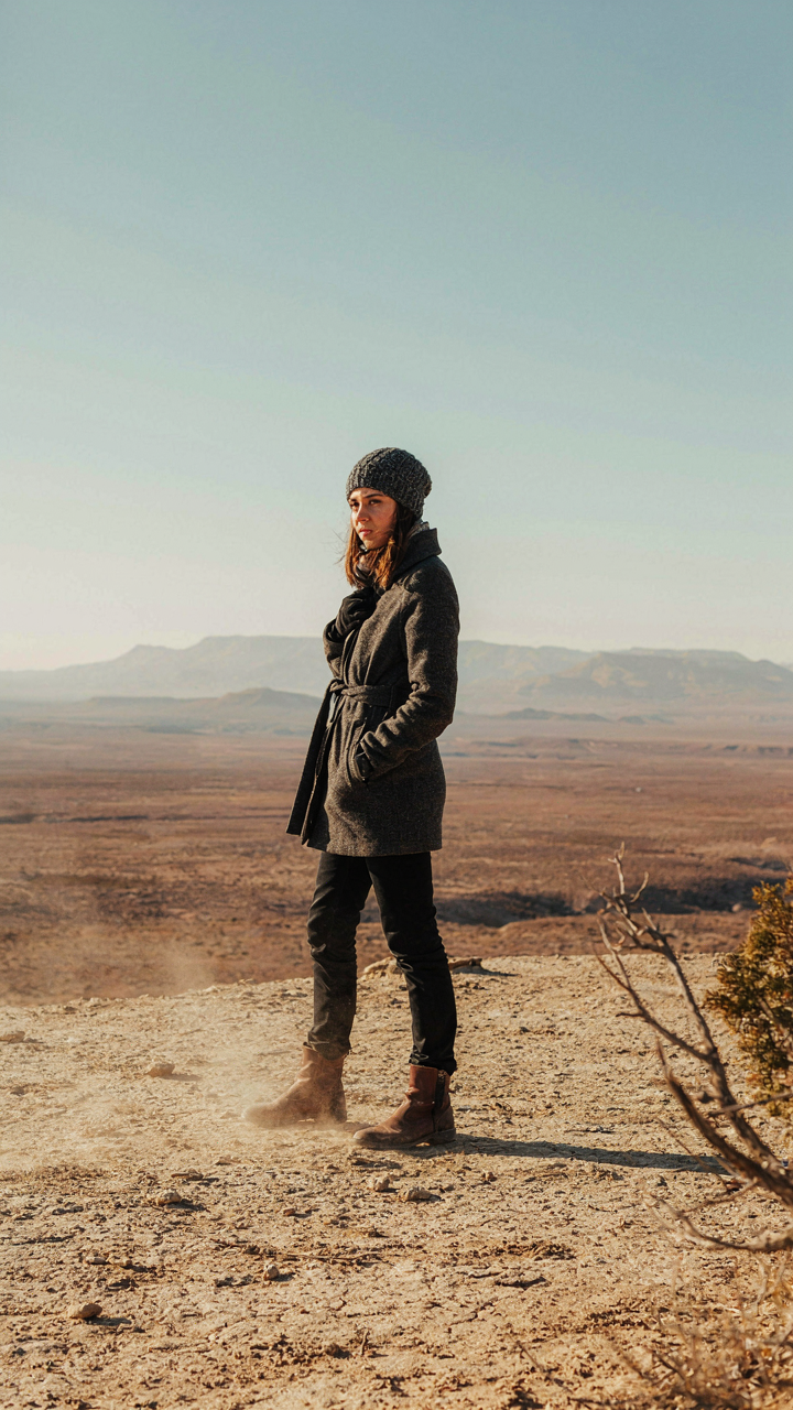 A person in a winter coat standing in a hot desert landscape.