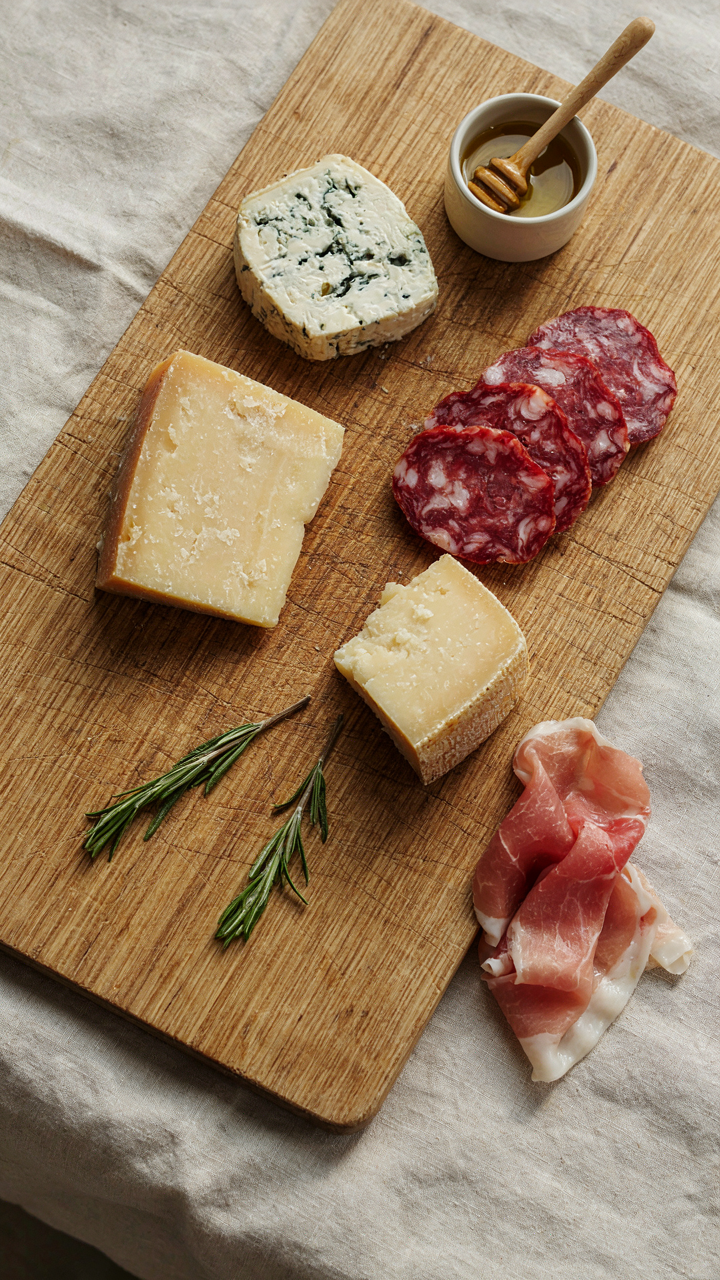 Hard cheeses and cured meats are arranged on an outdoor charcuterie board.