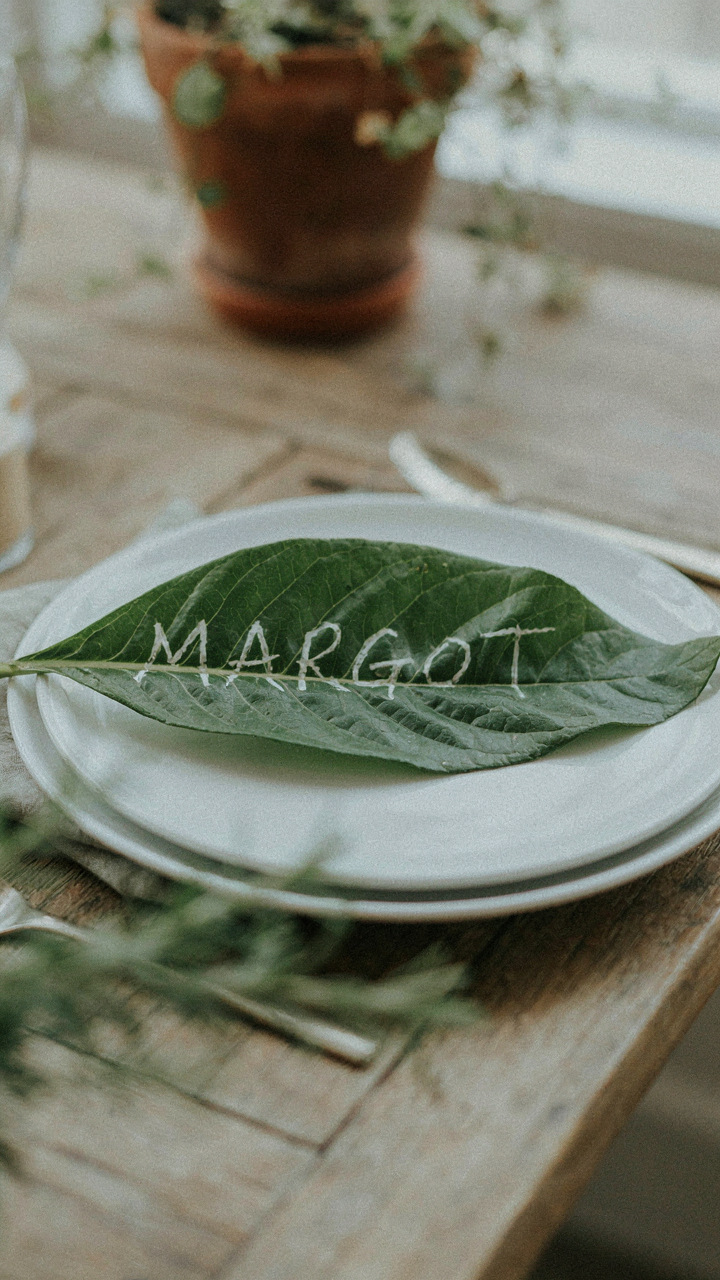 A large green leaf with a name written in white sits on a dinner plate.
