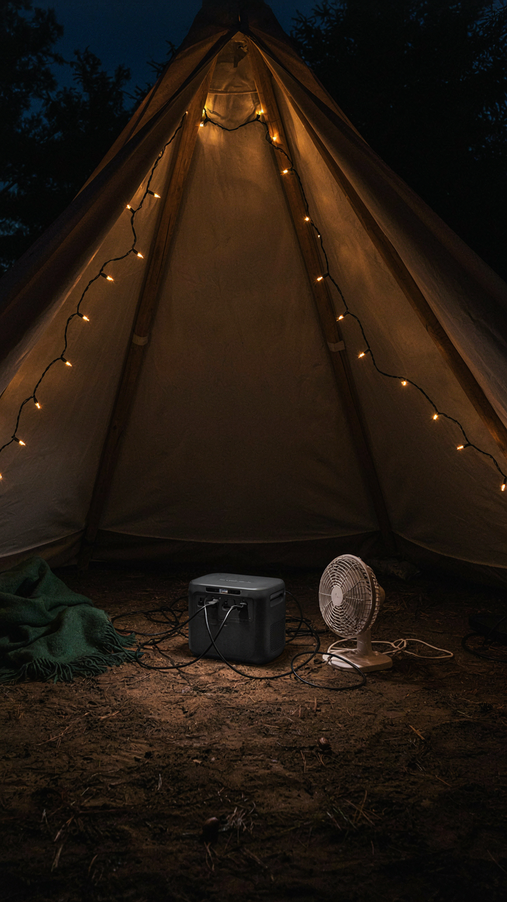 A portable power station charges lights and a fan inside a small backyard tent at night.