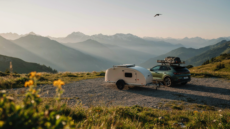 A compact SUV is parked with a small, aerodynamic teardrop camper at sunrise.