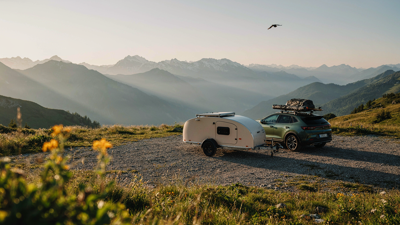A compact SUV is parked with a small, aerodynamic teardrop camper at sunrise.