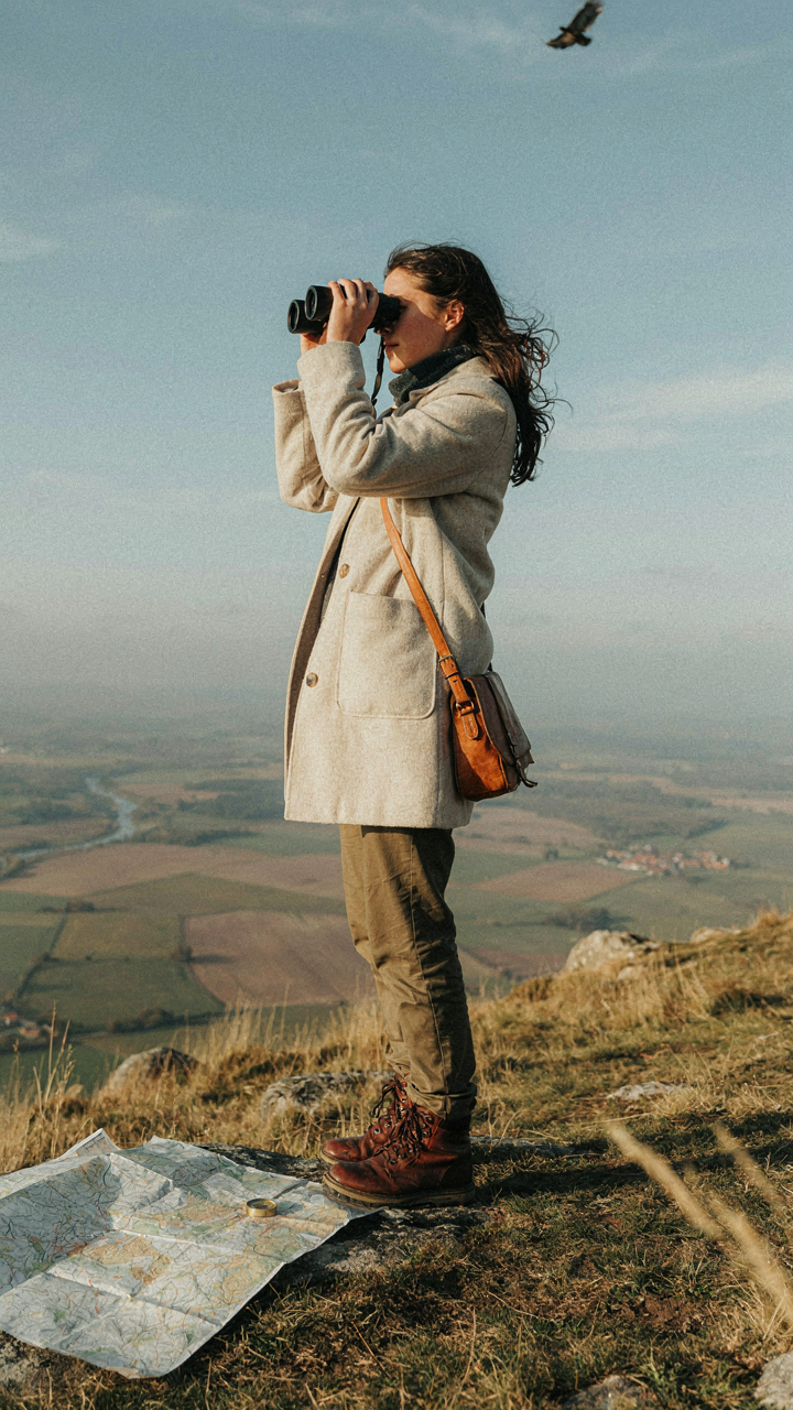 A person looks through binoculars at a landscape.