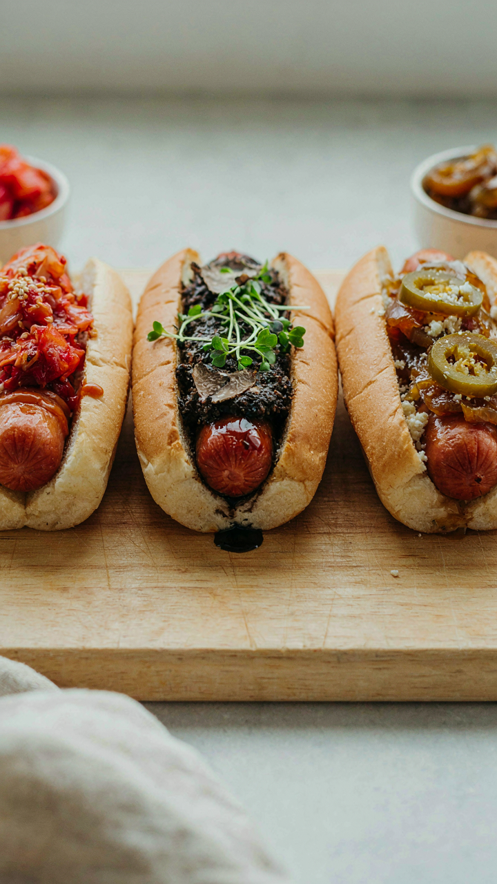Three identical hot dogs are shown with different and creative condiment pairings.
