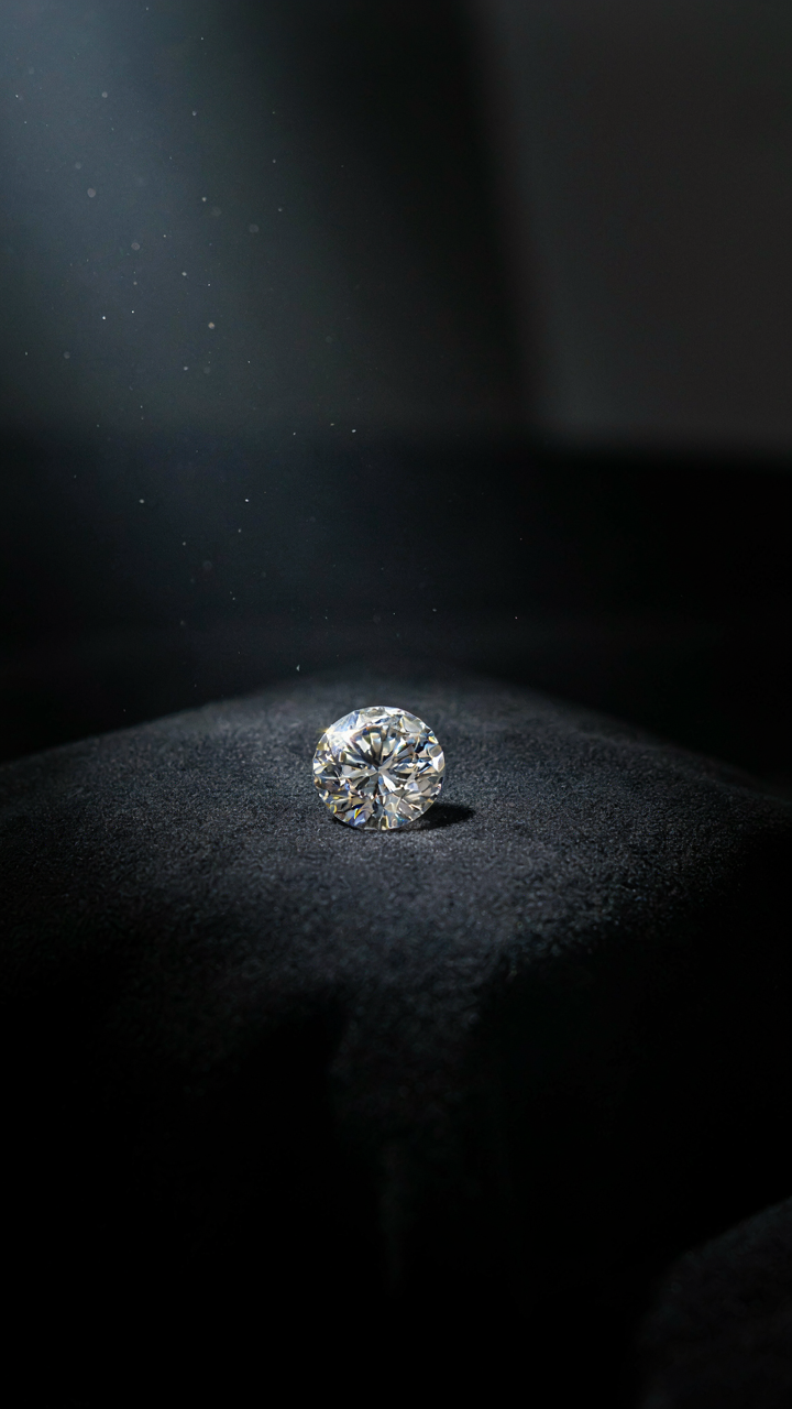 A single, perfectly cut diamond sits on a black velvet cushion.