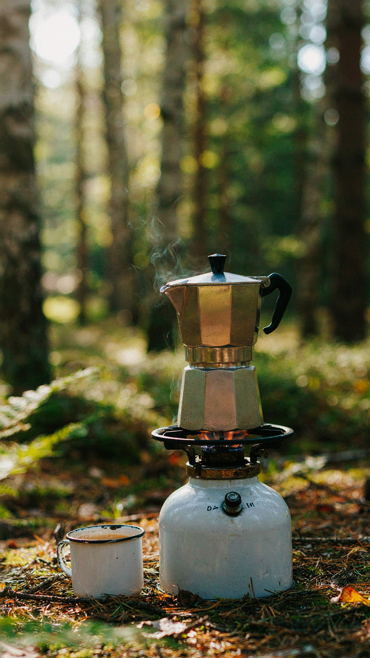 A classic Moka pot sits on a small camp stove, steaming gently.