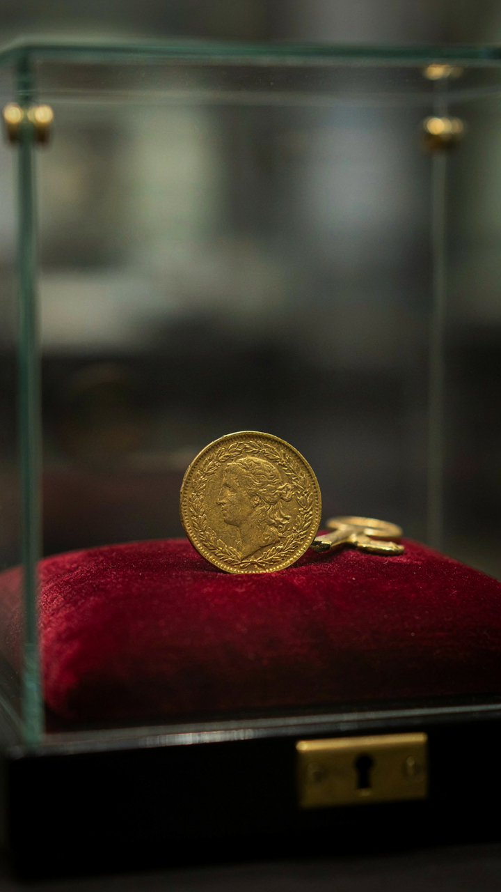 An antique gold coin on a velvet cushion in a glass case.