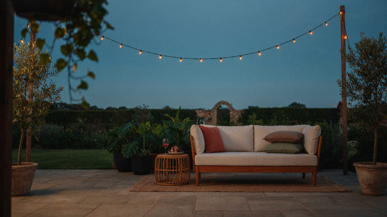 A well-lit patio with glowing outdoor string lights, comfortable furniture, and green plants.