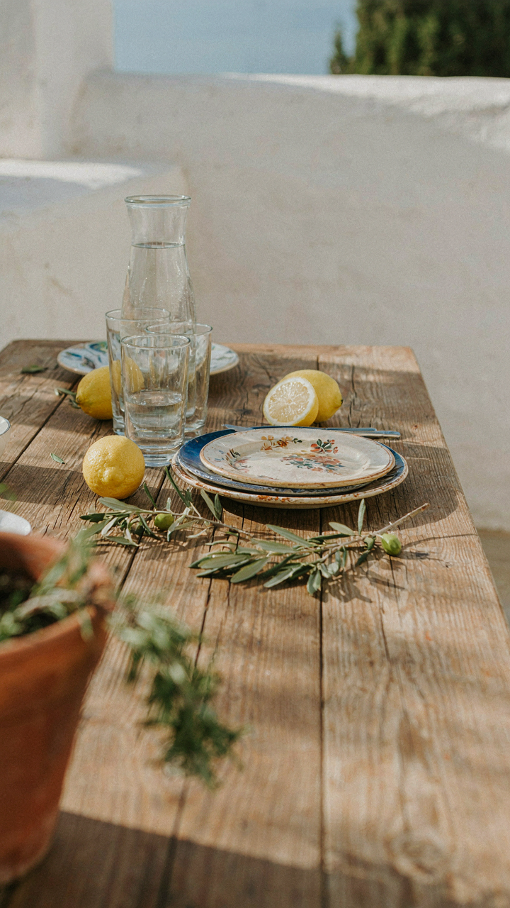 A rustic outdoor table setting with mismatched plates, lemons, and olive branches.