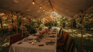 An elegant outdoor Thanksgiving dinner table set with warm blankets and string lights under a tent.