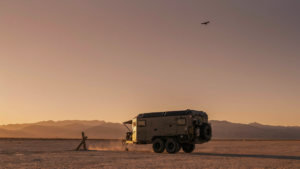 An overland trailer sits in a desert at sunset.