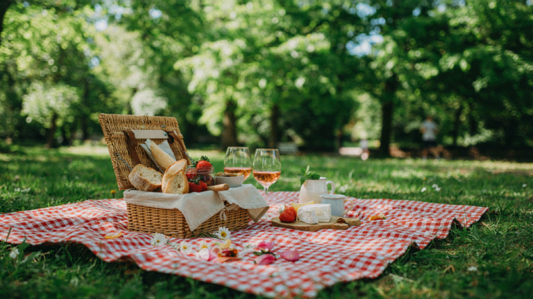 An open picnic basket sits on a red and white blanket filled with various picnic food ideas.