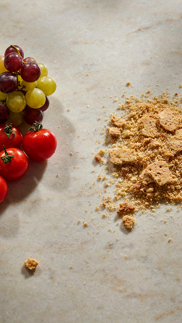 Smooth grapes and cherry tomatoes sit next to a pile of messy cracker crumbs.