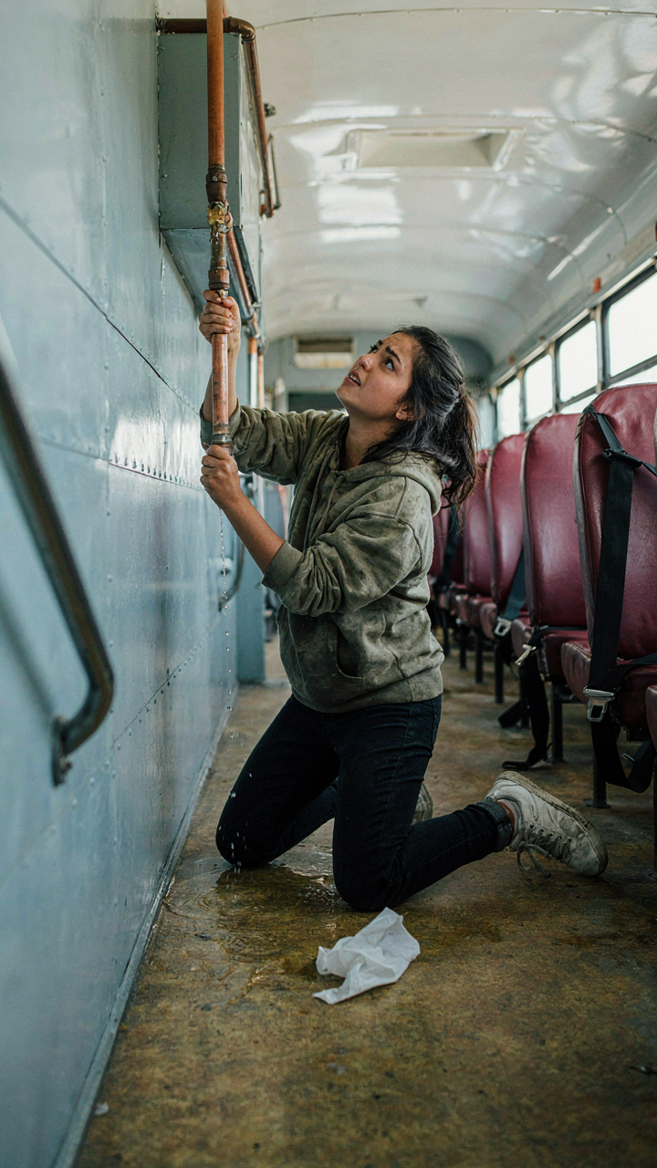 A leaky pipe in a school bus bathroom, dripping water on the floor.