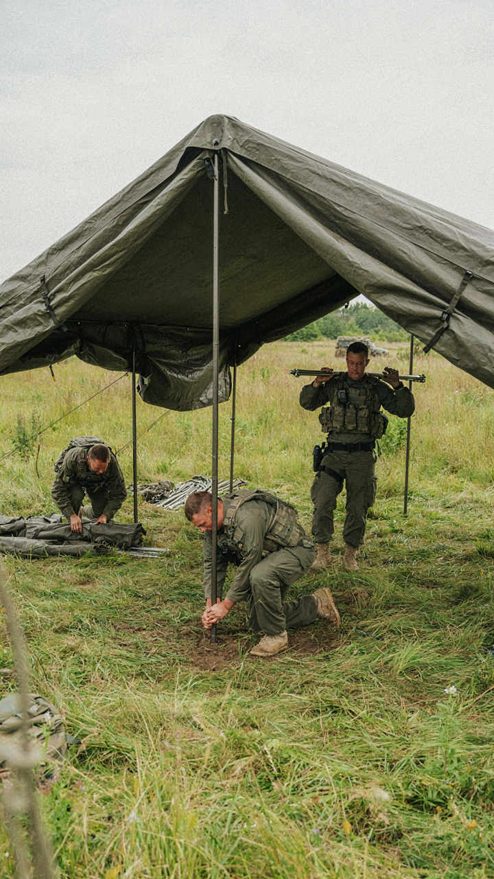Military personnel efficiently take down a large tactical tent.