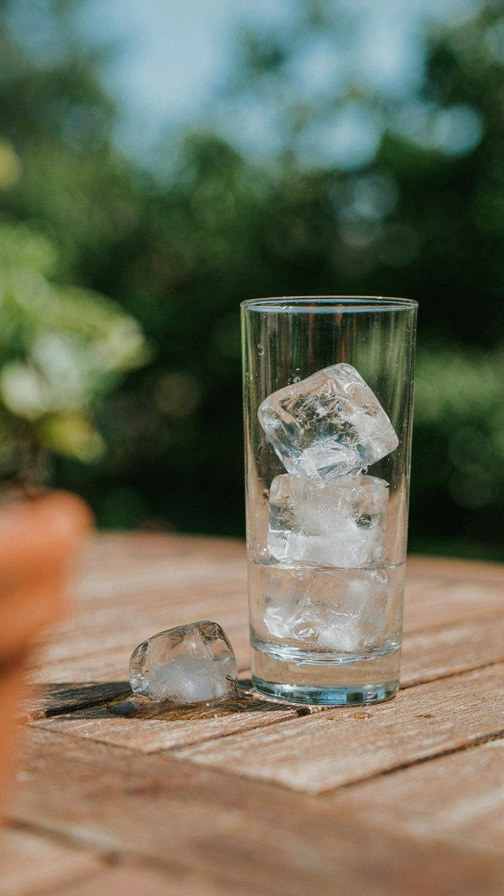 Ice cubes slowly melt in a clear glass on a hot outdoor table.