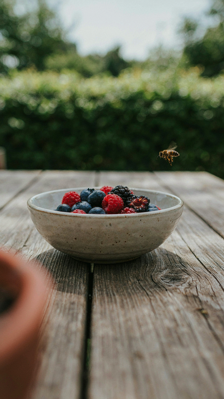 A weathered rustic outdoor table holds a single handmade ceramic bowl of berries.