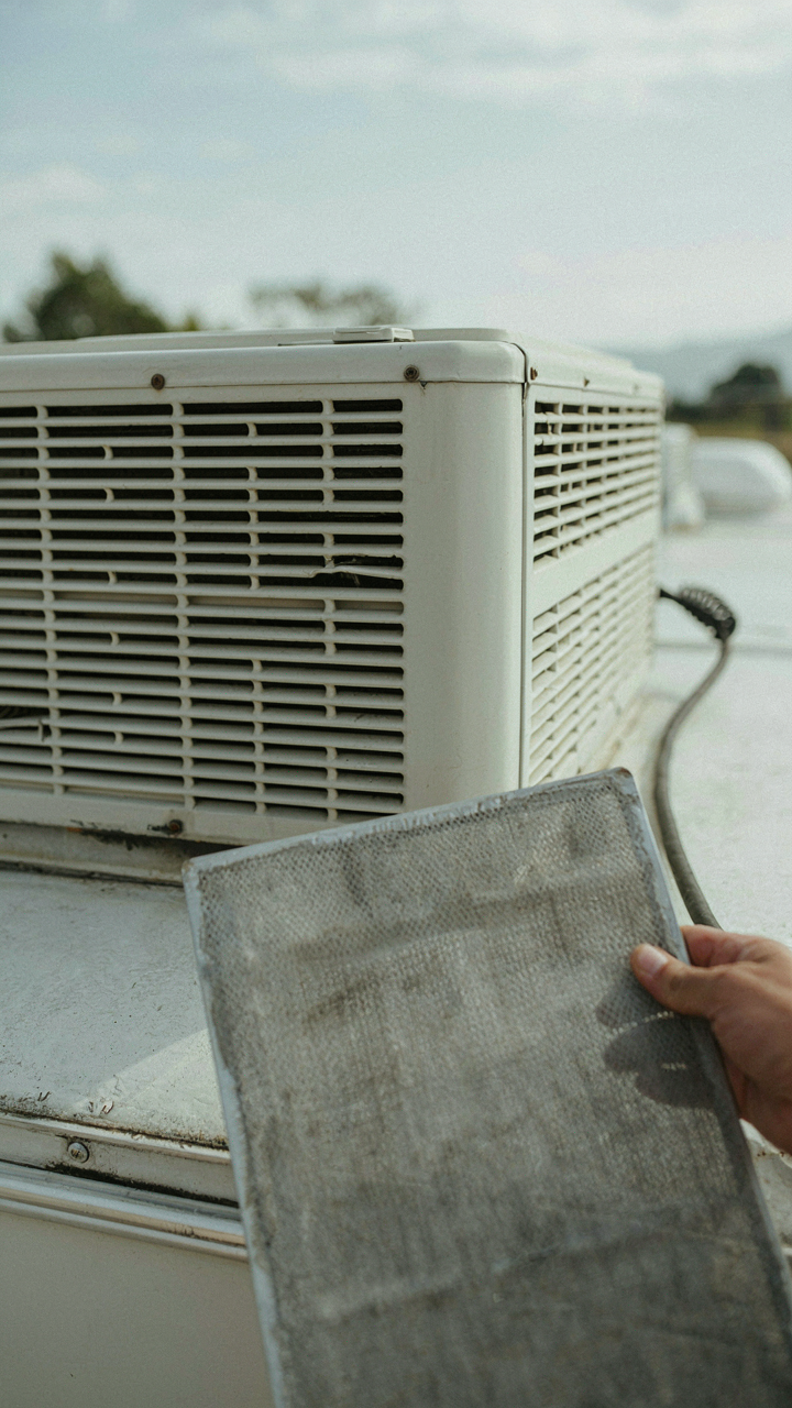 A hand cleans a filter on an RV air conditioner unit on the roof.