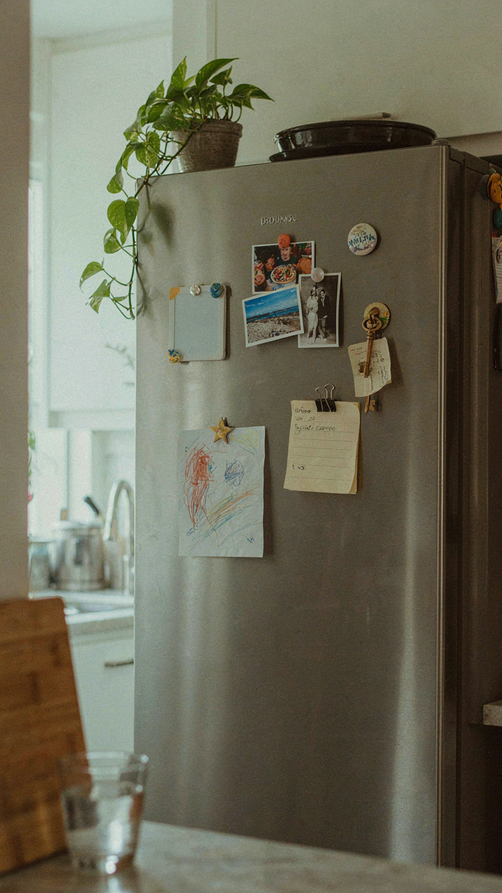 A refrigerator door is covered in colorful magnets holding papers.