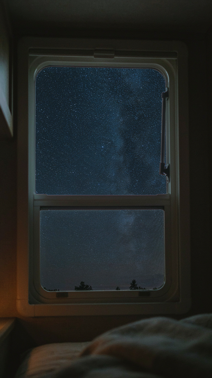 An open RV window with a mesh screen shows a cool, dark night sky.