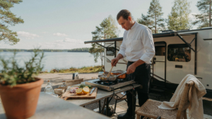 An rv outdoor kitchen setup with a person cooking near a lake.
