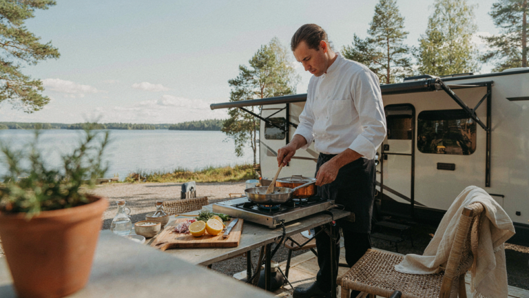 An rv outdoor kitchen setup with a person cooking near a lake.