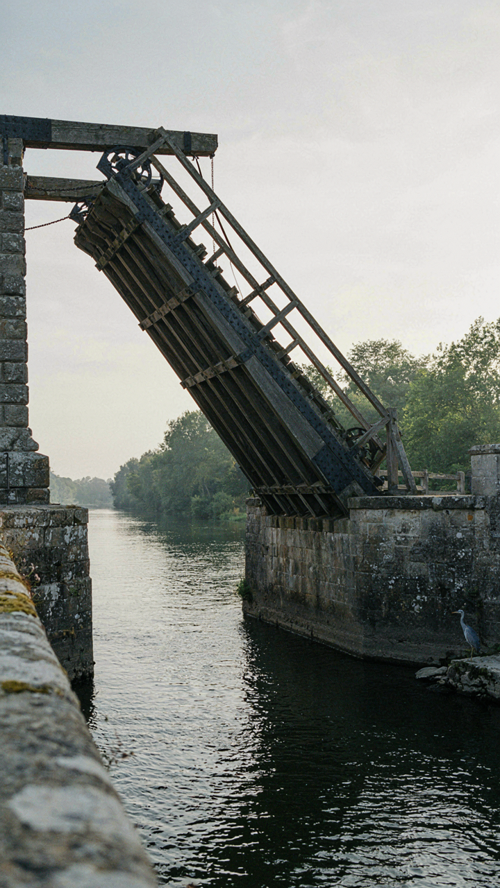 An old drawbridge slowly lifts, creating a gap over water.