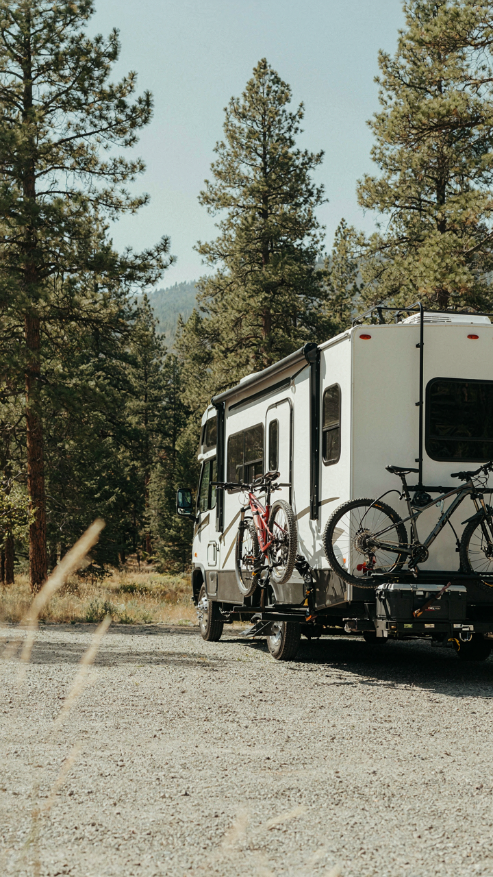 A fifth-wheel RV with bikes and a storage box on a rear cargo carrier.