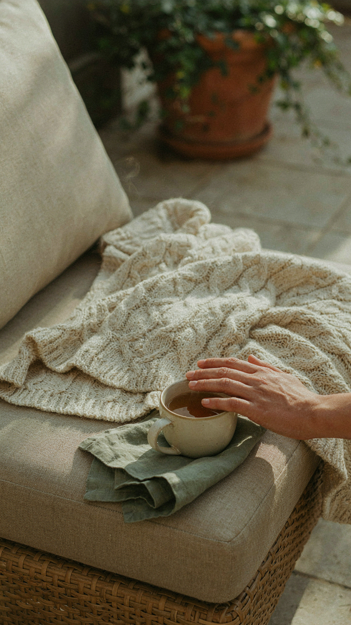 A hand gently touching a soft, textured throw blanket on an outdoor sofa.