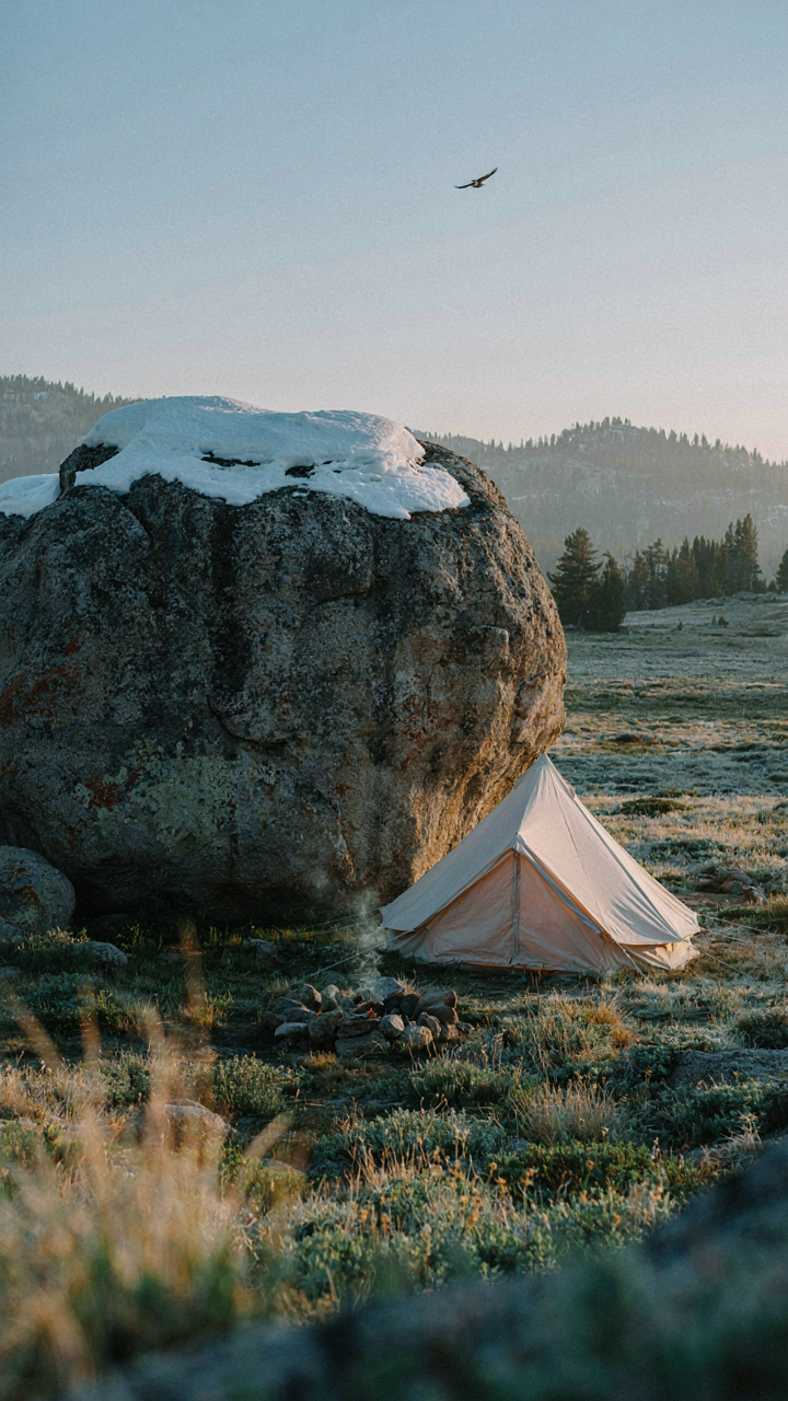 A glamping tent sits behind a big snow-covered rock, blocking the wind.