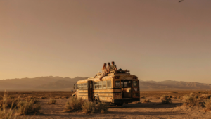 A skoolie roof deck with people enjoying a desert sunset from above their bus.
