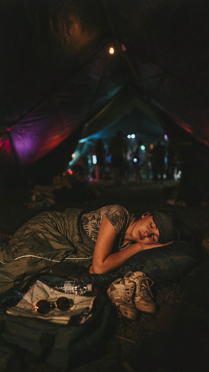 Inside a darkened festival tent, a person sleeps with earplugs and an eye mask.