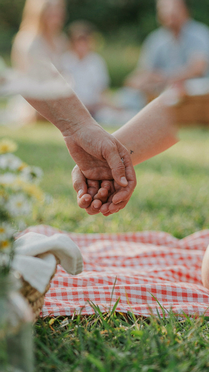 An adult's hand holding a child's hand on a simple picnic blanket.