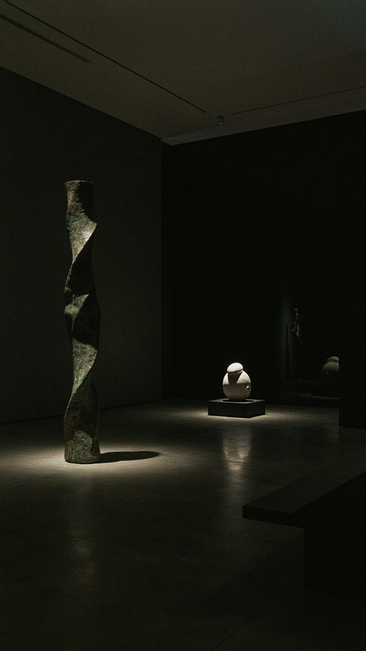 Spotlights in an art gallery highlight sculptures, creating shadows.