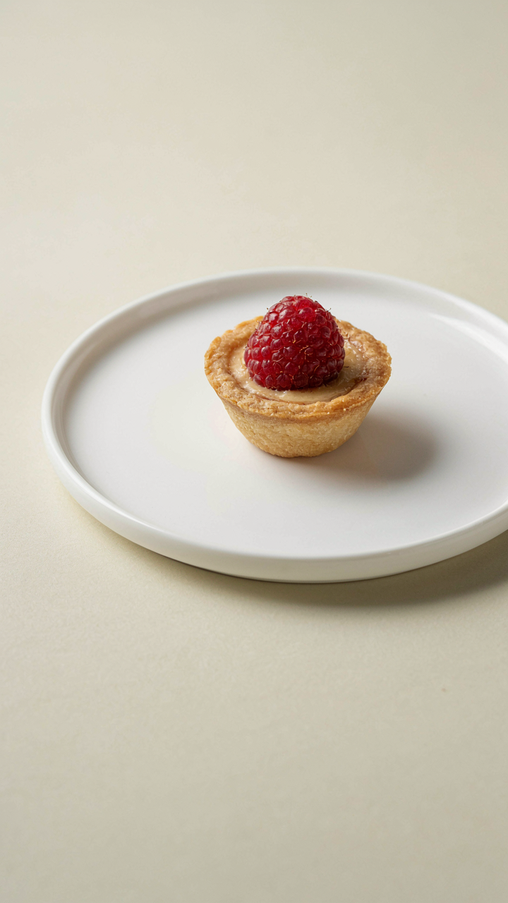 A small, elegant berry tart on a white plate with plenty of empty space.