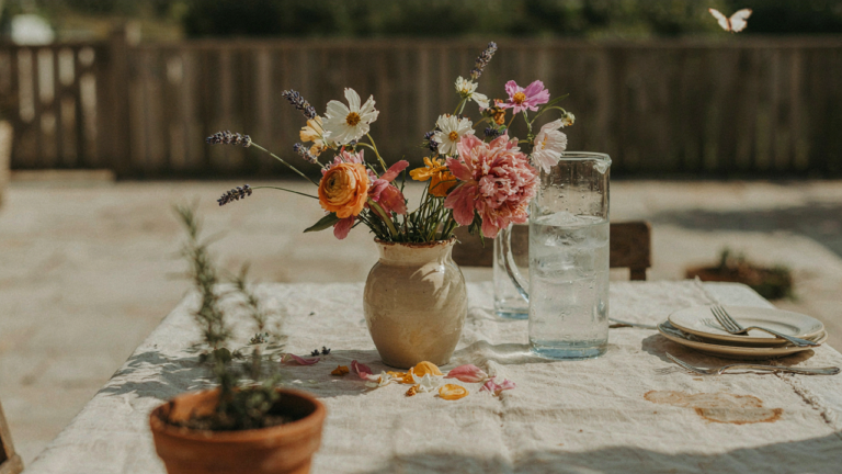 A wilting summer tablescape with flowers, melting ice, and a rumpled tablecloth.
