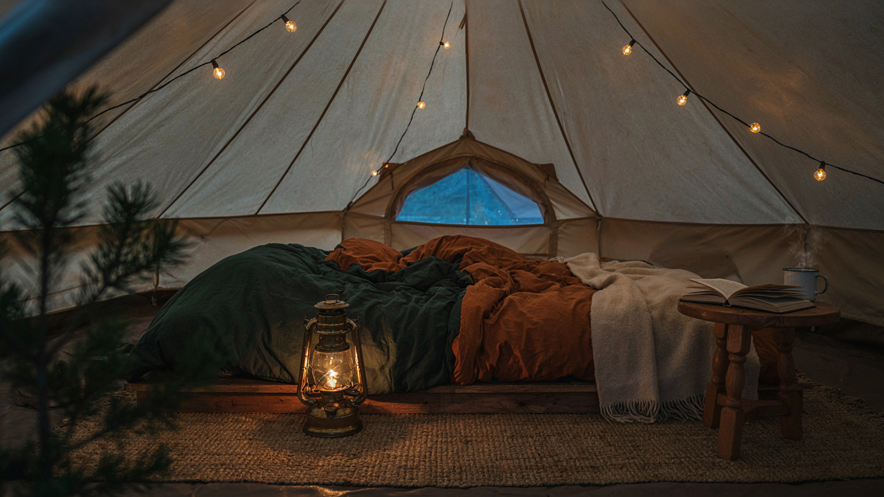 A warm tent interior at dusk with string lights and a small lantern.