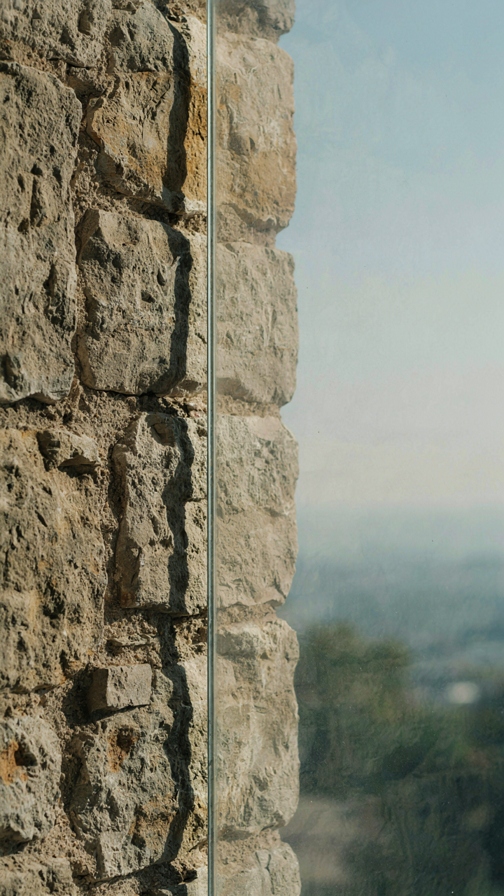 A close-up of a rough stone wall next to a smooth glass surface.