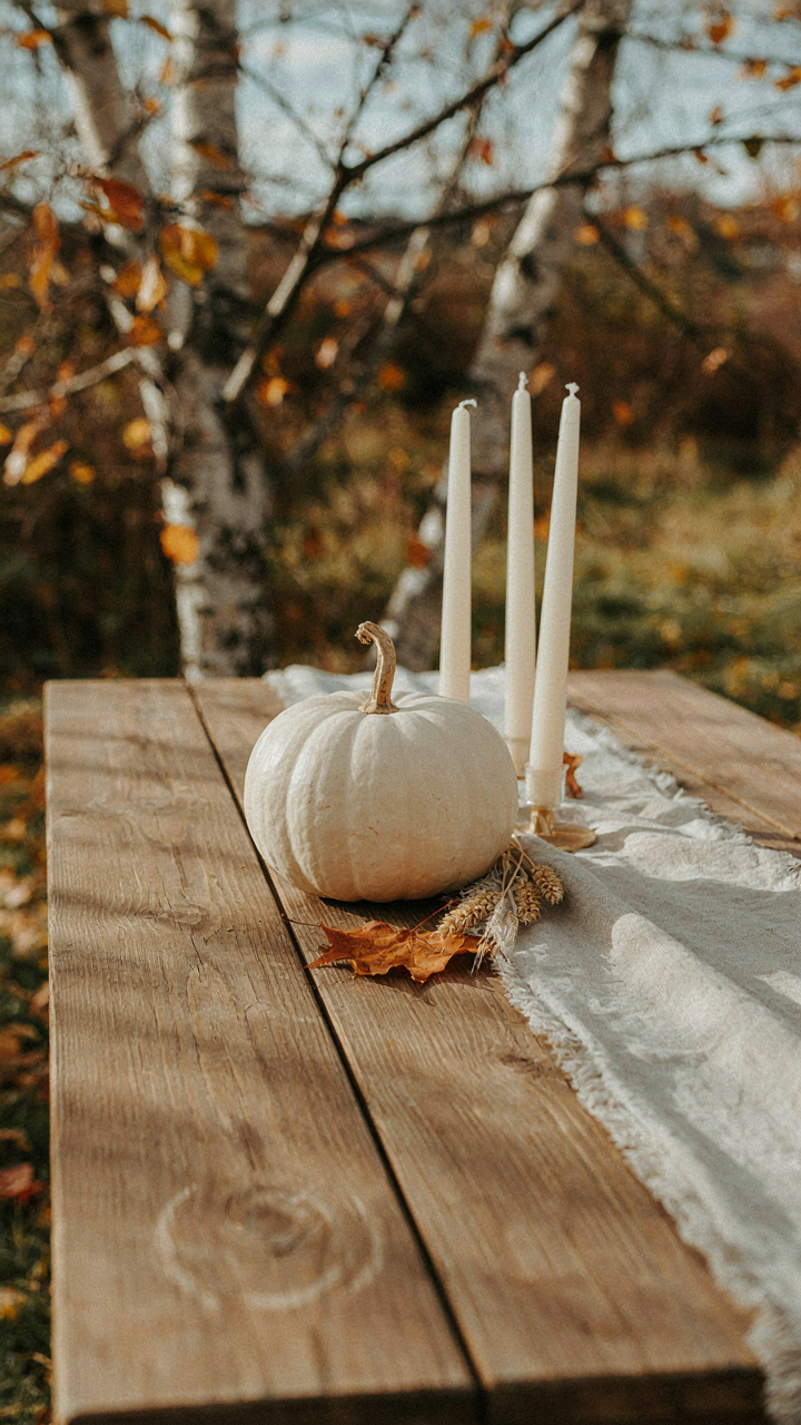 A minimalist fall outdoor tablescape has a single ceramic pumpkin and two elegant candles.