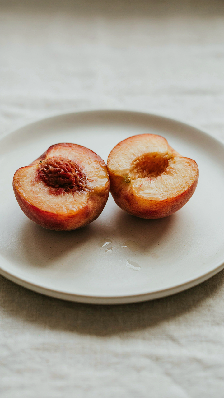 A ripe, juicy peach cut in half on a simple white plate.