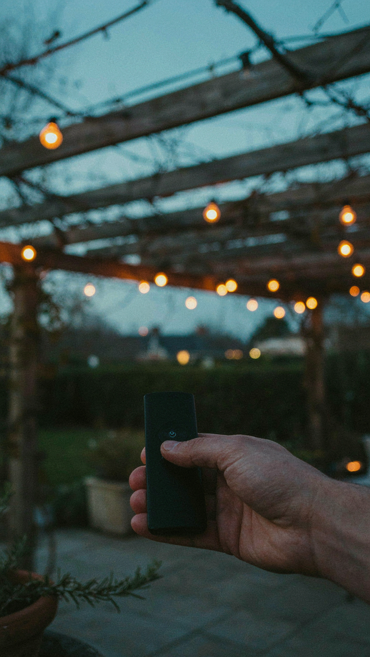 A hand using a remote to control string lights over a pergola.