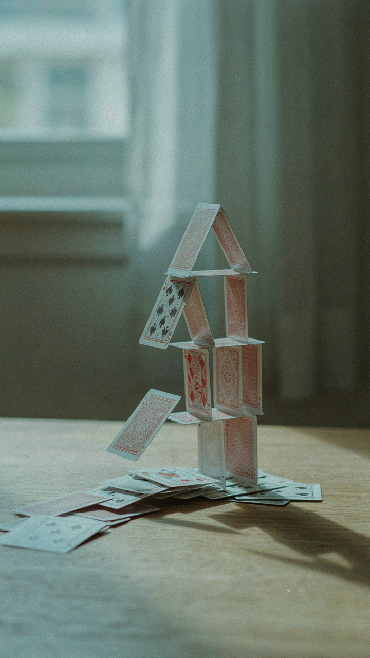 A delicate house of cards is collapsing, with many pieces falling.