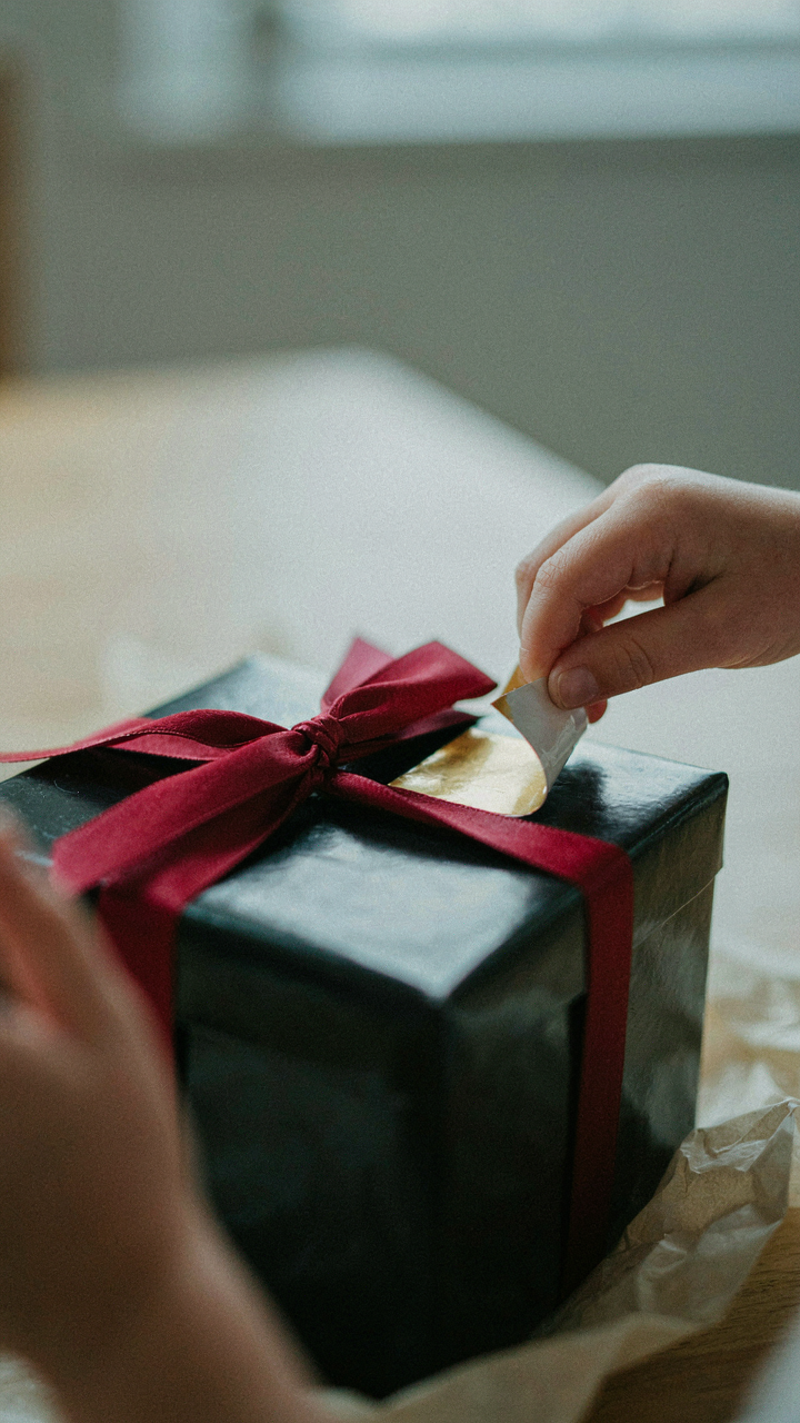 A child's hand tries to peel a cheap sticker off a gift box.