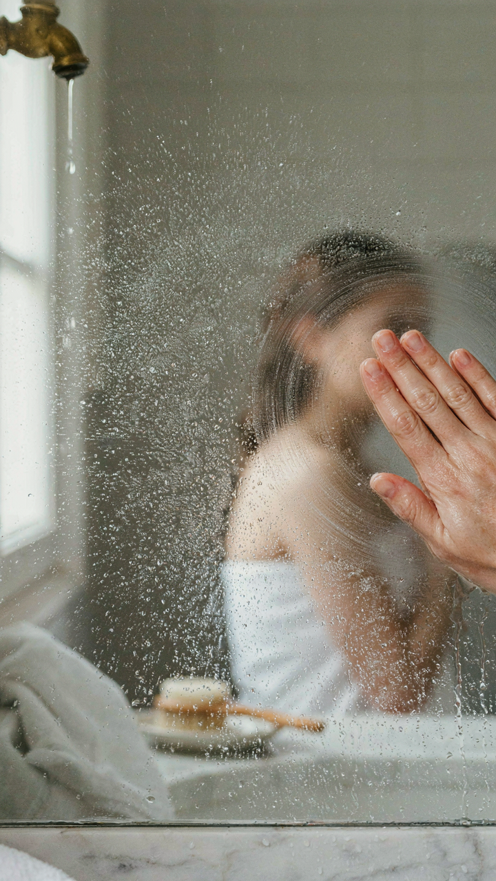 A hand wipes away steam from a bathroom mirror after a hot shower.