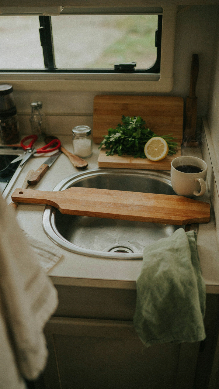 An RV sink is barely visible under a cutting board and many kitchen items.