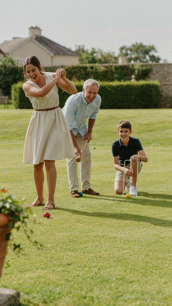 People are laughing and playing a vibrant game of croquet on a manicured lawn.